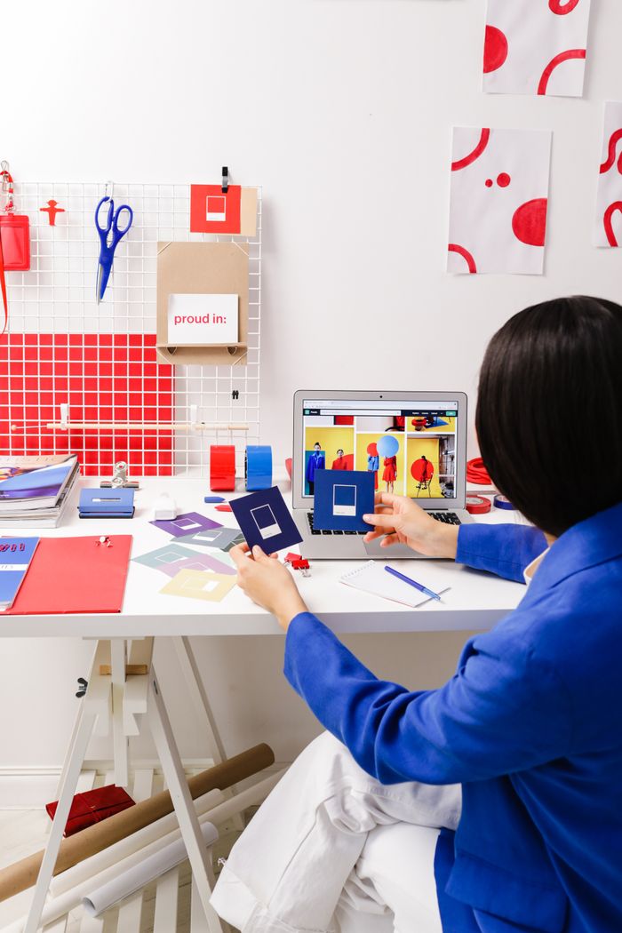 Designer in a blue jacket working on color samples at a desk with laptop and tools.
