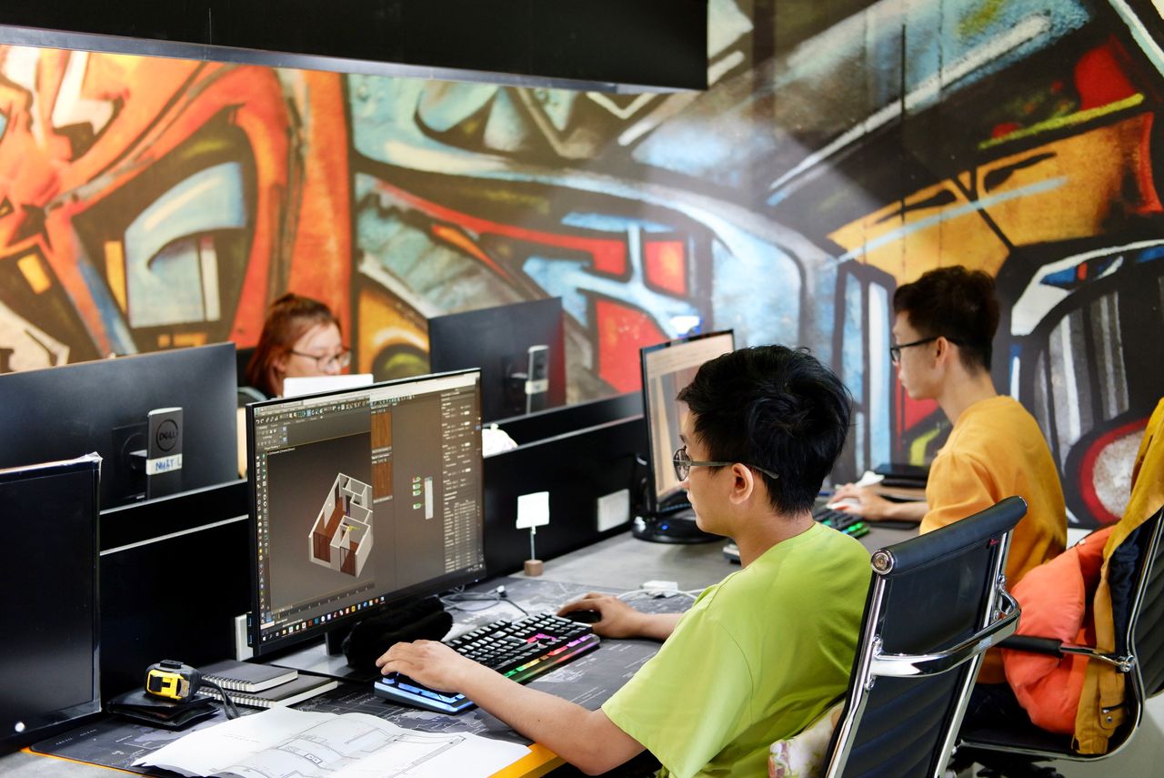 Three young people working on computers in a creative office with vibrant graffiti walls.